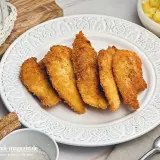 Knusprige Hähnchenstreifen in goldbrauner Panko Panade auf einem Teller, daneben Kartoffelsalat.