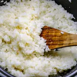 Frisch gekochter Reis wird mit einem Holzlöffel vermischt, bereit für Sushi-Essig.