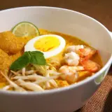 Schüssel mit cremigem Laksa-Rezept, Garnelen, Ei, frischen Sprossen und Limette.