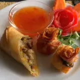 Knusprige Frühlingsrollen und Teigtaschen mit süß-saurer Sauce, garniert mit Karottenblumen. Ein köstlicher Nam Prik Genuss.