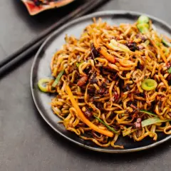 Ein Teller mit dampfendem Lo Mein, garniert mit Karotten und Frühlingszwiebeln, bereit zum Genießen mit Stäbchen.