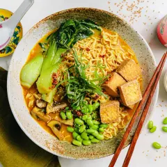 Schüssel mit Ramen-Nudeln, Bok Choy, Pilzen, Edamame und Tofuwürfeln. Die Vielfalt der **ramen toppings** macht dieses Gericht unwiderstehlich.