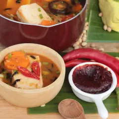 Gochujang Zutaten: Ein Topf mit Tofu-Eintopf, eine Schüssel mit scharfem Eintopf, rote Chilis, Sojabohnen und ein Block Tofu auf Bananenblättern.