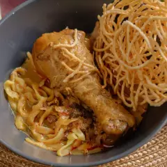 Khao Soi: ein Hühnerbein auf Nudeln in cremiger Kokosmilch-Currysauce, garniert mit knusprigen Nudeln.