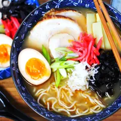 Eine Schüssel Ramen mit perfekt gekochten ramen eiern, Schweinefleisch, Bambussprossen und Frühlingszwiebeln. Daneben liegen weitere halbe Eier.