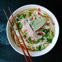 Eine Schüssel dampfendes Pho mit dünnen Rindfleischscheiben, Reisnudeln, Frühlingszwiebeln und Chili. Ein perfektes Pho-Rezept für kalte Tage.