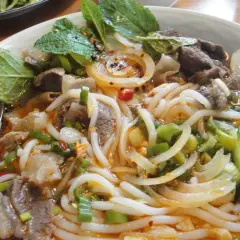 Eine Schüssel Bun Bo Hue mit Rindfleisch, Nudeln, Zwiebeln, Frühlingszwiebeln und Minze.