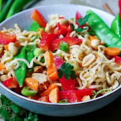 Bunter mie nudelsalat mit Erdnüssen, Paprika, Zuckerschoten und Karotten, garniert mit Petersilie.