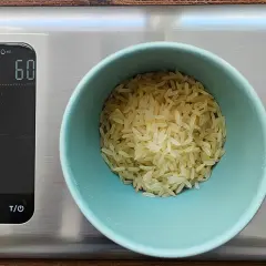 Eine Waage zeigt 60g Reis an. So behältst du die Reis Kalorien im Blick.