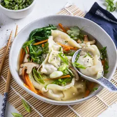Eine dampfende Schüssel **Wantan Suppe** mit zarten Teigtaschen, Shiitake-Pilzen, Karotten und Frühlingszwiebeln, garniert mit Sesam.