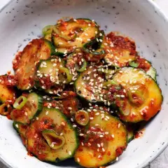 Ein Schüssel mit einem würzigen Gurken-Kimchi-Salat, garniert mit Sesam und Frühlingszwiebeln.