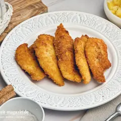 Knusprige Hähnchenstreifen in goldbrauner Panko Panade auf einem Teller, daneben Kartoffelsalat.