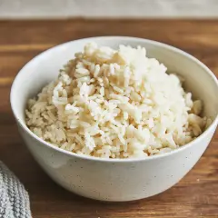 Eine Schüssel mit dampfendem parboiled Reis steht auf einem Holztisch. Daneben liegt ein graues Stofftuch.