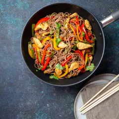 Wok-Gericht mit chinesischen Eiernudeln, Hähnchenstreifen und bunten Paprikastreifen, garniert mit Koriander.