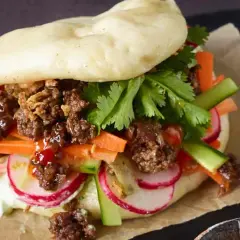 Ein saftiger Bao Burger mit Hackfleisch, knackigem Gemüse wie Karotten, Radieschen und Gurken, garniert mit Koriander.