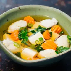 Eine Schüssel Hu Tieu Suppe mit Tofu, Karotten und Fleischbällchen, garniert mit Frühlingszwiebeln und Petersilie.