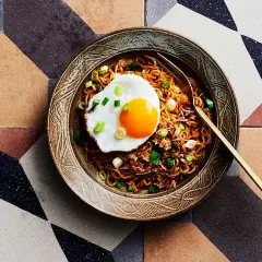 Schüssel mit Mie Goreng, garniert mit einem Spiegelei und Frühlingszwiebeln, auf einem geometrischen Fliesenmuster.