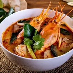 Eine Schüssel Tom Yum Suppe mit Garnelen, Pilzen und Kaffirlimettenblättern, garniert mit Koriander.