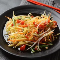 Ein bunter Papaya Salat mit Karottenstreifen, Kirschtomaten und Sprossen, serviert auf einem schwarzen Teller mit roten Stäbchen.
