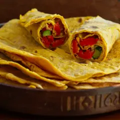 Chapati-Rezept: Fladenbrot gefüllt mit roten Paprika und Gurke, auf einem Stapel weiterer Chapati in einer Holzschale.