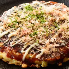 Ein herzhaftes Okonomiyaki Hiroshima, übergossen mit Sauce und Mayonnaise, bestreut mit Bonitoflocken und Schnittlauch.