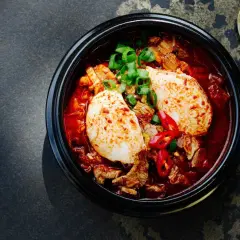 Herzhaftes Kimchi Jjigae mit Tofu, Rindfleisch und Frühlingszwiebeln, garniert mit Chilischeiben.
