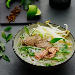 Eine dampfende Schüssel Pho Suppe mit zarten Rindfleischscheiben, Reisnudeln, Sojasprossen und frischen Kräutern.