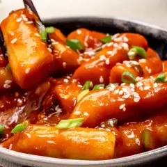 Schüssel mit würzigem Tteokbokki, Reiskuchen in scharfer Sauce, garniert mit Sesam und Frühlingszwiebeln.