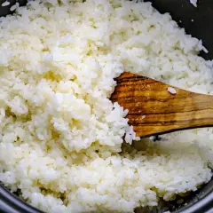 Frisch gekochter Reis wird mit einem Holzlöffel vermischt, bereit für Sushi-Essig.