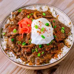 Eine köstliche japanische Bowl mit Reis, zartem Rindfleisch, einem pochierten Ei, eingelegtem Ingwer und Frühlingszwiebeln.