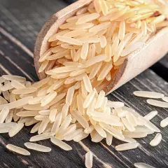 Ein Holzlöffel voller heller Reiskörner, die auf einer dunklen Holzoberfläche verstreut sind. Dies ist ein Beispiel für Rundkornreis.
