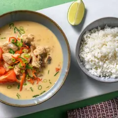 Khao tom: Eine Schüssel mit cremigem Hühner-Kokos-Eintopf, garniert mit Tomaten und Frühlingszwiebeln, daneben eine Schüssel Reis und eine Limettenspalte.
