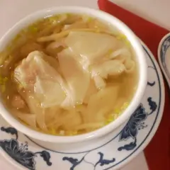 Eine Schüssel mit dampfender Wan-Tan-Suppe, gefüllt mit zarten Teigtaschen und Garnelen, bereit zum Genießen.