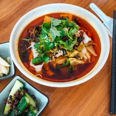 Eine Schüssel Niu Rou Mian, garniert mit Koriander, daneben eingelegte Gurken und Rettich.