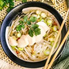 Eine dampfende Schüssel vietnamesische Reissuppe mit zarten Hühnerbrustscheiben, Reisnudeln, Sojasprossen und Frühlingszwiebeln.