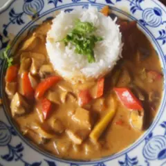 Ein Curry mit Hühnchen, Pilzen und Paprika, serviert mit duftendem asiatischem Reis auf einem blumengemusterten Teller.