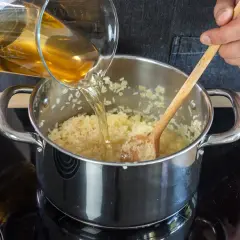 Flüssigkeit wird in einen Topf mit pilaw reis gegossen, während mit einem Holzlöffel gerührt wird.