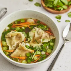 Eine Schüssel mit dampfender Suan La Tang, gefüllt mit Teigtaschen, Karottenstreifen und Frühlingszwiebeln.