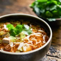 Eine dampfende Schüssel Miso Suppe mit Tofu, Nudeln und Frühlingszwiebeln, garniert mit frischer Petersilie.