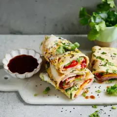 Gestapelte Jian Bing mit Schinken, Käse und Paprika, garniert mit Koriander und Sesam. Dazu eine Schale dunkler Sauce.
