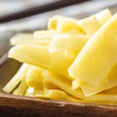 Holzschale mit leuchtend gelben, geschnittenen Bambussprossen, die gesund und appetitlich aussehen. Ein dunkler Löffel liegt im Hintergrund.