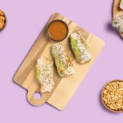 Frische Sommerrollen mit Hoisin-Sauce, Garnelen, Avocado und Erdnüssen auf lila Hintergrund.