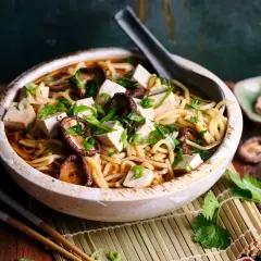 Herzhaftes Shiitake Ramen mit Tofuwürfeln und Frühlingszwiebeln in einer tiefen Schüssel, garniert mit Koriander.