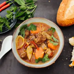 Herzhaftes Bo Kho, ein vietnamesischer Rindfleischeintopf mit Karotten und Sternanis, serviert mit Baguette und frischen Kräutern.