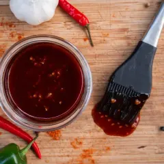 Hoisin-Sauce verwendung: eine Schüssel mit dunkler Sauce, dane ein Pinsel, dane rote Chilis und Knoblauch. Perfekt für Marinaden und Glasuren.