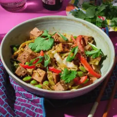 Schüssel mit spitzkohl asiatisch vegetarisch, Tofu, Edamame und Koriander. Dazu Stäbchen und ein Glas Wasser.