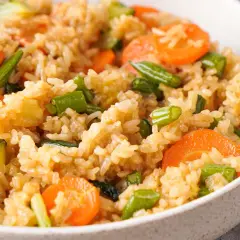 Reispflanze mit Karotten, Zucchini und grünen Bohnen in einer Schüssel, ein gesundes und farbenfrohes Gericht.