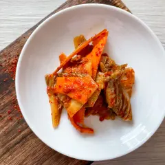 Frisch zubereitetes Kimchi, ein köstliches Rezept, serviert auf einem weißen Teller mit karamellisierten Karottenstreifen und Chinakohl.