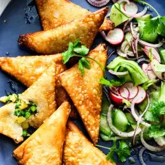 Goldbraune, knusprige Samosas mit Erbsen- und Kartoffelfüllung, serviert mit einem frischen Gurken-Radieschen-Salat. Ein leckeres samosas rezept.
