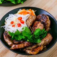 Bun cha Hanoi: gegrilltes Schweinefleisch und Fleischbällchen mit Reisnudeln, Kräutern und Chili auf einem Teller.